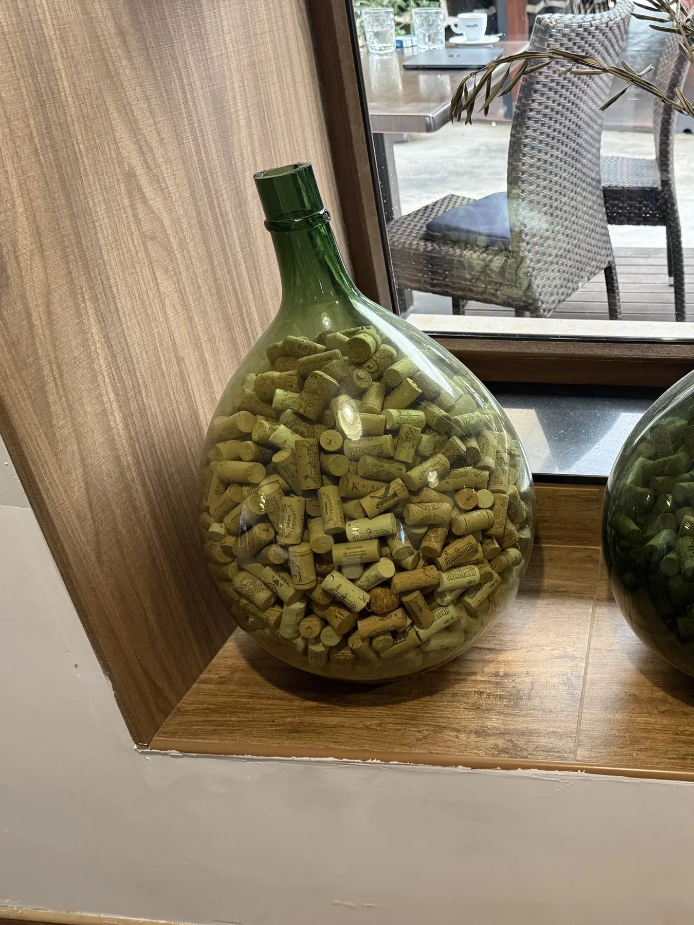Staklena demižona puna čepova od vina u prozorskoj niši, s pogledom na terasu