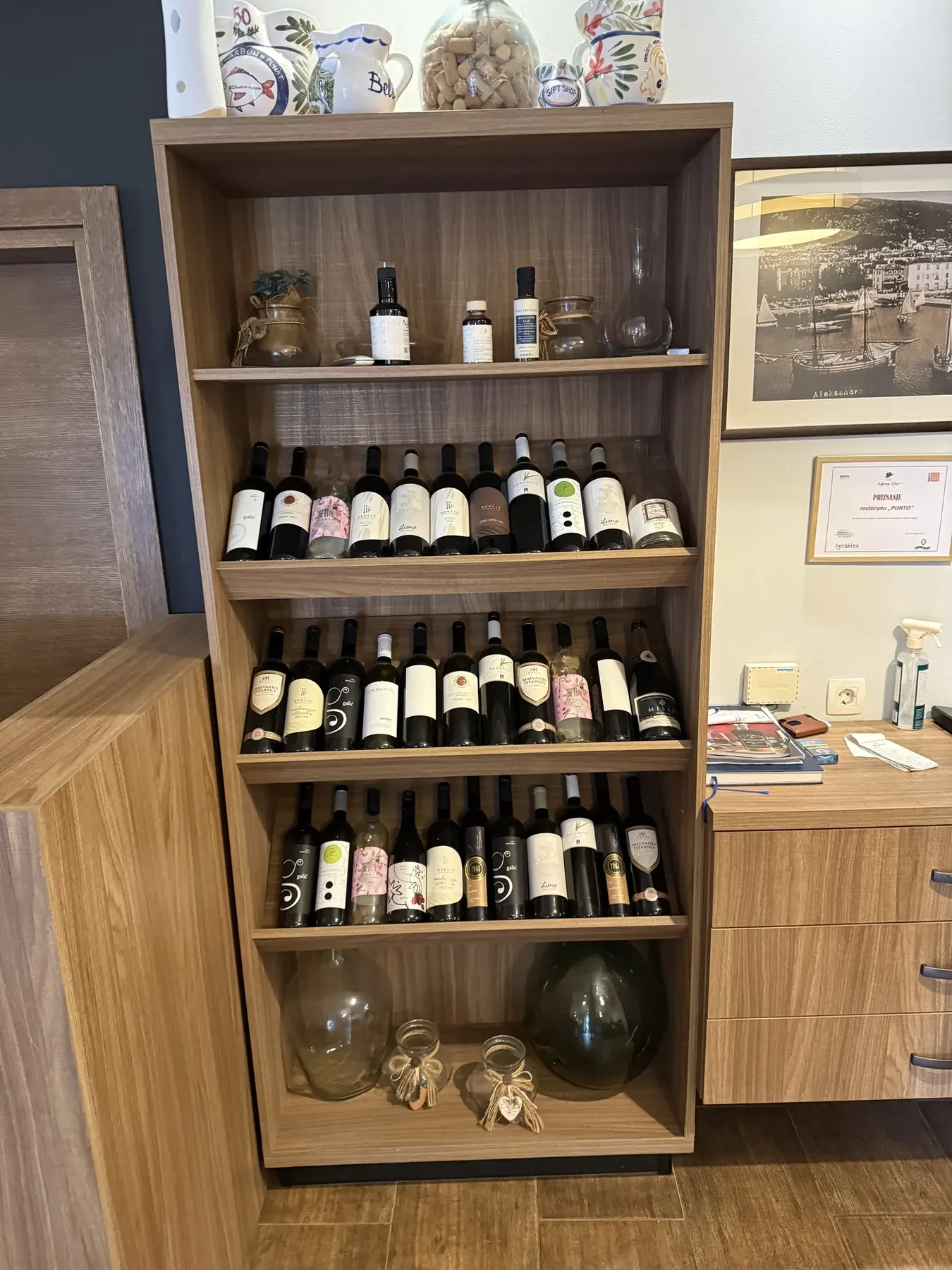 Vinski ormar restorana Punto, s keramičkim vrčevima na vrhu i priznanjem na zidu